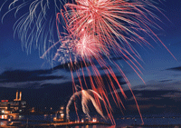 Fireworks exploding in the night sky over water.