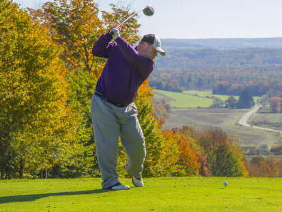 Man golfing overlooking valley with colorful fall foliage all around