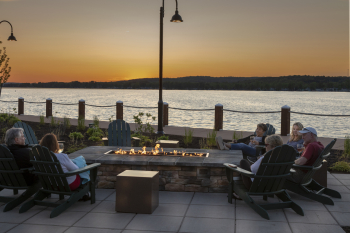 Friends gathered around a fire pit at the Chautauqua Harbor Hotel at dusk. Chautauqua Lake in the background