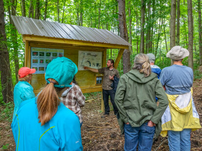 A group of people on a nature hike, looking at a sign in the woods