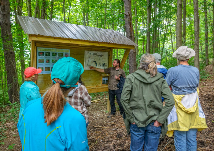 A group of people on a nature hike, looking at a sign in the woods