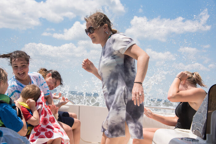 Family group laughing on a pontoon boat as waves wet them