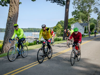 A group of cyclists riding past Chautauqua Lake, waiving