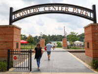 Comedy Center Park sign with people walking underneath toward train tracks