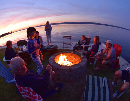 people gathered around a campfire at sunset near a lake