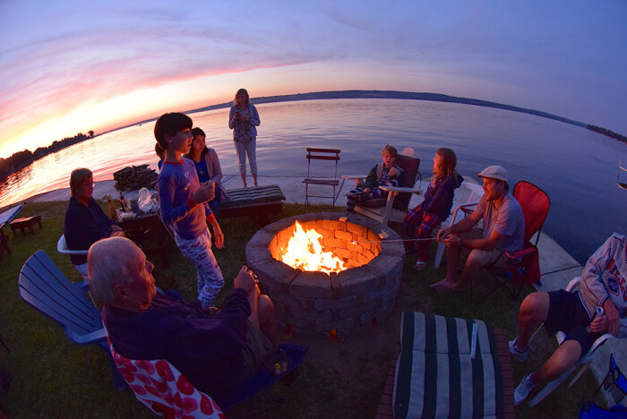 people gathered around a campfire at sunset near a lake