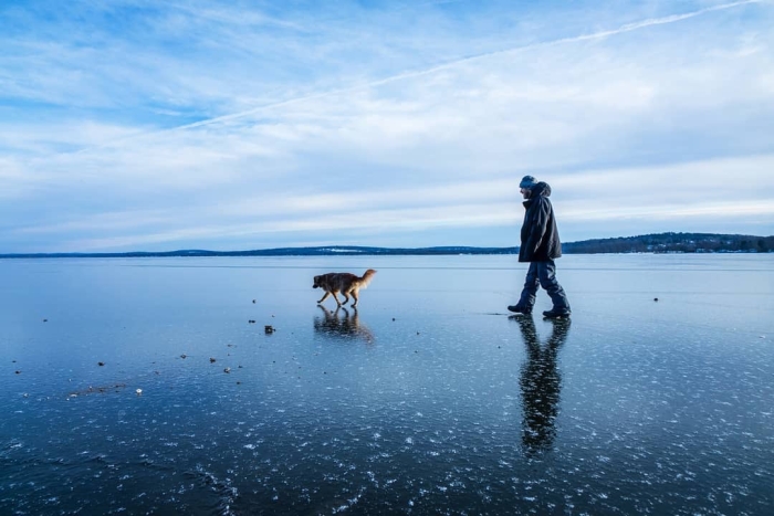 Man and dog walking on a glassy, frozen Chautauqua Lake