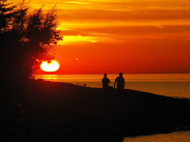 Sunset and a silhouette of two campers at lakeside campground.